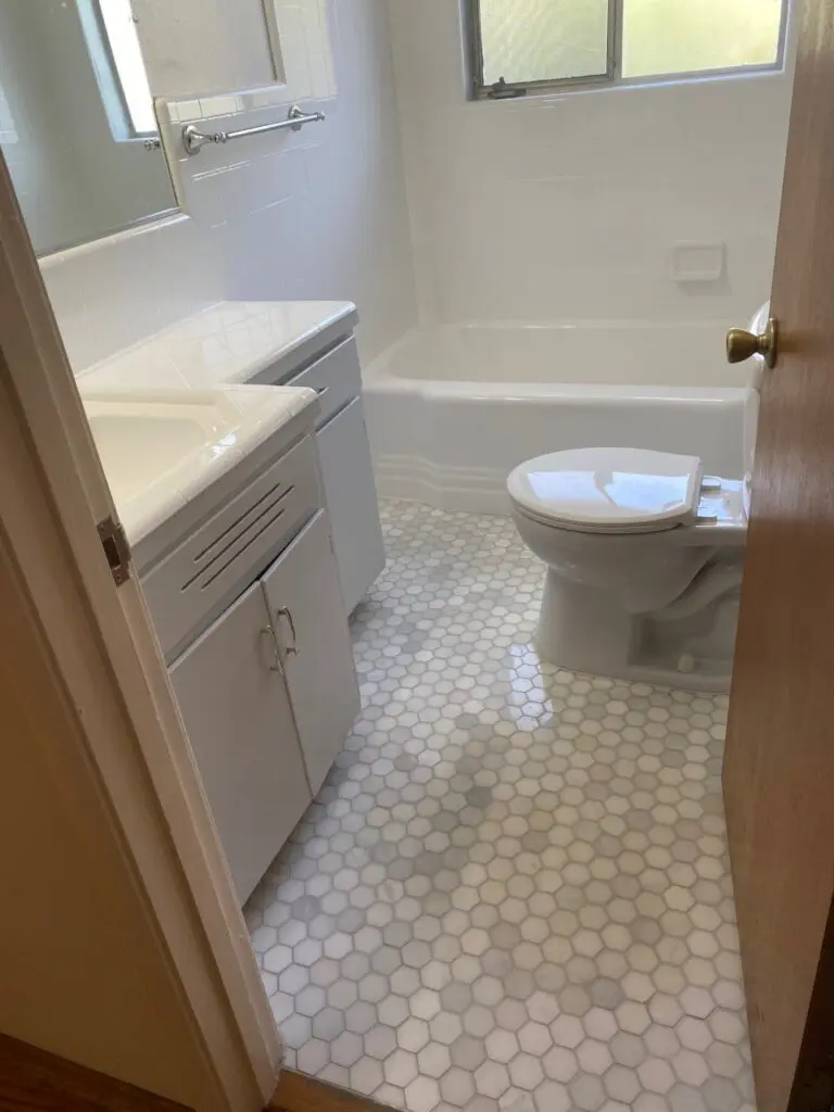 a bathroom with white tiles, a white tub, a white sink, and a white toilet